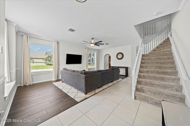 living area with ceiling fan, stairs, arched walkways, and crown molding