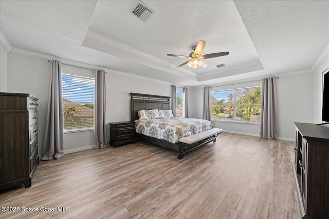 bedroom with light wood-style floors, a tray ceiling, visible vents, and ornamental molding