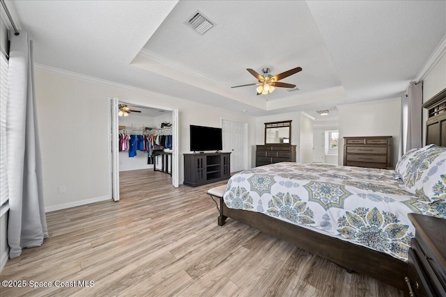 bedroom featuring light wood finished floors, a raised ceiling, visible vents, and crown molding