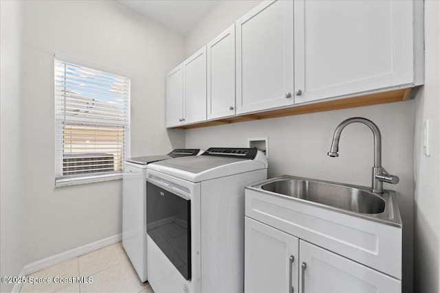 clothes washing area featuring light tile patterned flooring, a sink, baseboards, independent washer and dryer, and cabinet space