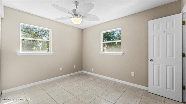 empty room featuring light tile patterned flooring, a ceiling fan, and baseboards