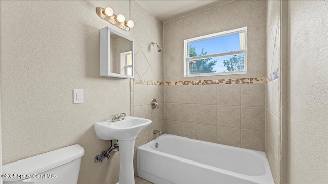 bathroom featuring shower / washtub combination, a textured wall, and toilet