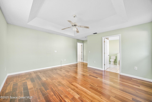 unfurnished room featuring a raised ceiling, light wood-style flooring, and baseboards