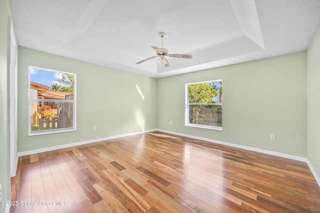 unfurnished room featuring a ceiling fan, a tray ceiling, baseboards, and wood finished floors