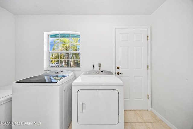 clothes washing area with light tile patterned floors, laundry area, washing machine and clothes dryer, and baseboards