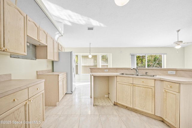 kitchen featuring a sink, visible vents, light countertops, freestanding refrigerator, and light brown cabinetry