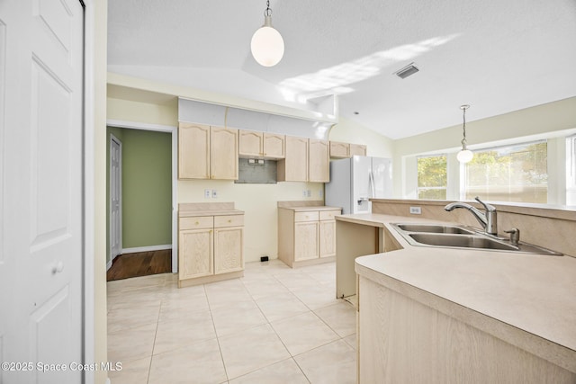 kitchen featuring lofted ceiling, visible vents, light brown cabinets, a sink, and white fridge with ice dispenser