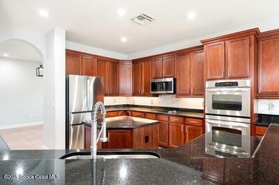 kitchen featuring stainless steel appliances, dark stone counters, a sink, and arched walkways