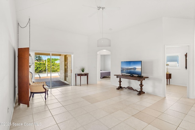 living area with arched walkways, light tile patterned floors, a towering ceiling, and a ceiling fan