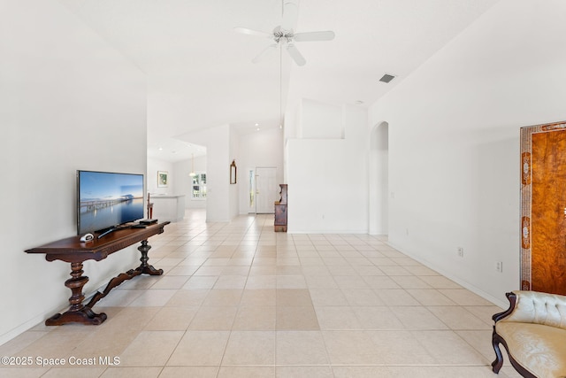 living area with visible vents, arched walkways, a ceiling fan, a towering ceiling, and light tile patterned flooring