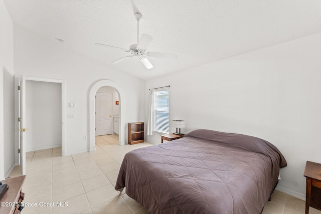 bedroom featuring lofted ceiling, light tile patterned flooring, arched walkways, and a textured ceiling