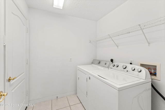 laundry area featuring light tile patterned floors, a textured ceiling, washing machine and dryer, laundry area, and baseboards