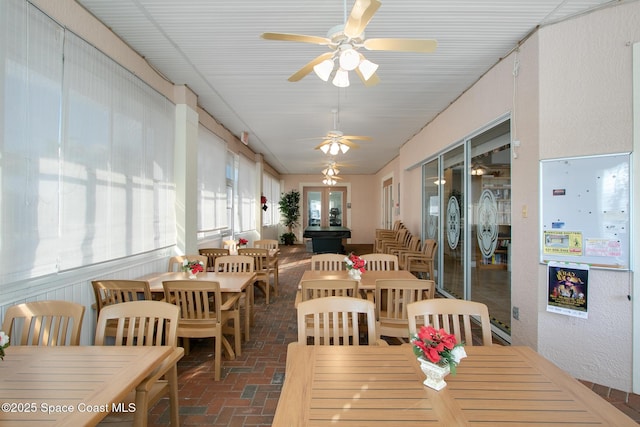 dining area with brick floor, a ceiling fan, and a sunroom