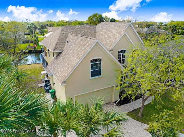 view of side of home with roof with shingles, an attached garage, and stucco siding