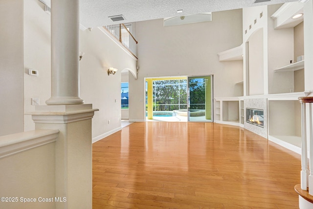 unfurnished living room with a textured ceiling, visible vents, built in features, hardwood / wood-style floors, and a tiled fireplace