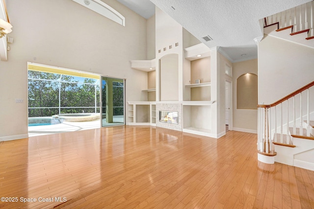 unfurnished living room with a textured ceiling, built in shelves, a tile fireplace, hardwood / wood-style flooring, and baseboards