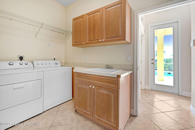 clothes washing area with a sink, light tile patterned floors, washing machine and dryer, and cabinet space