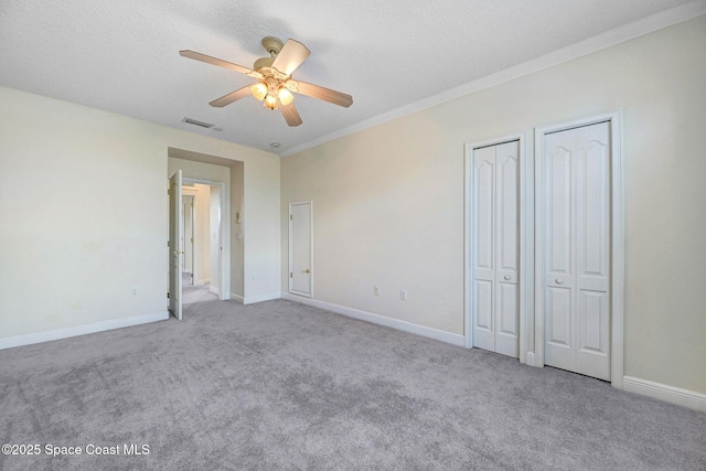 unfurnished bedroom with multiple closets, carpet flooring, a textured ceiling, and baseboards