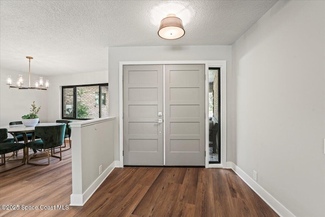 foyer entrance featuring dark wood-type flooring, a notable chandelier, a textured ceiling, and baseboards