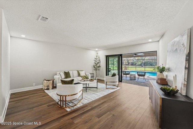 living room with baseboards, visible vents, a sunroom, wood finished floors, and a textured ceiling