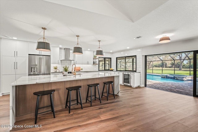 kitchen with stainless steel fridge, visible vents, wall chimney exhaust hood, wine cooler, and white cabinetry