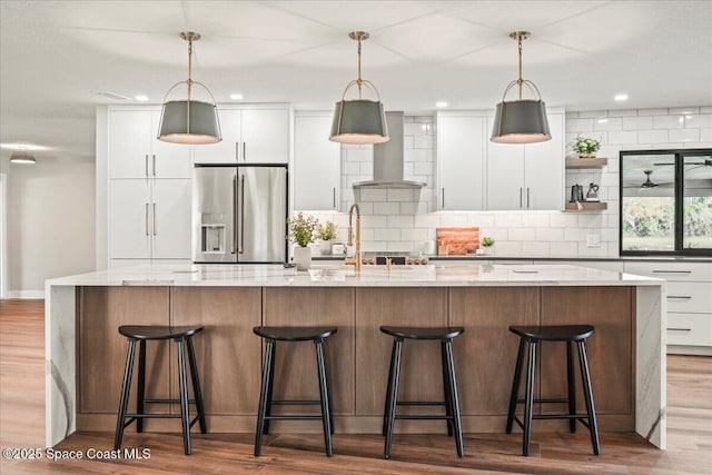 kitchen with tasteful backsplash, stainless steel fridge, wall chimney range hood, and white cabinetry