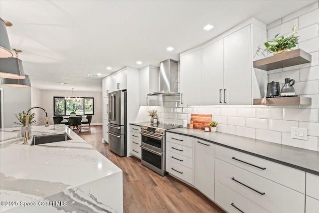 kitchen featuring appliances with stainless steel finishes, a sink, wall chimney range hood, open shelves, and backsplash