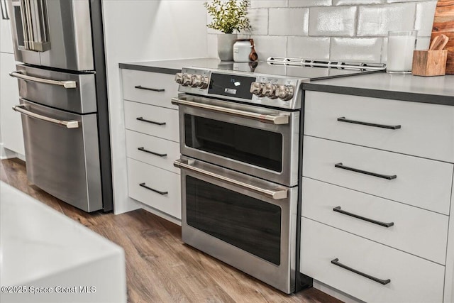 kitchen with white cabinets, appliances with stainless steel finishes, backsplash, dark countertops, and dark wood finished floors