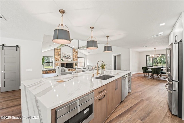 kitchen with a barn door, a sink, open floor plan, appliances with stainless steel finishes, and light wood-type flooring