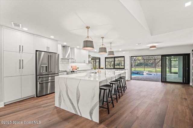 kitchen featuring wood finished floors, visible vents, appliances with stainless steel finishes, wall chimney exhaust hood, and tasteful backsplash