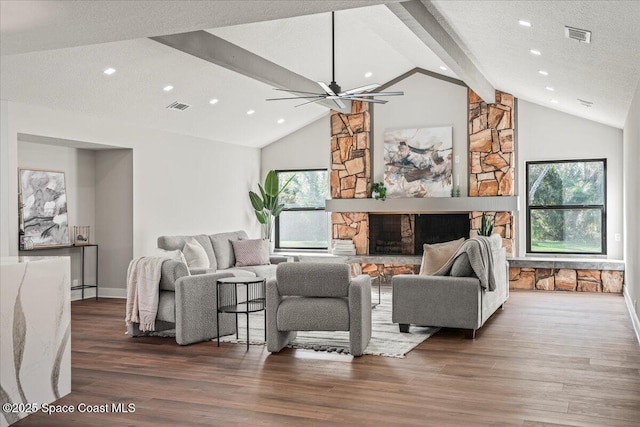 living area featuring a textured ceiling, a stone fireplace, wood finished floors, and visible vents