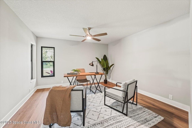 office featuring light wood-type flooring, a ceiling fan, baseboards, and a textured ceiling