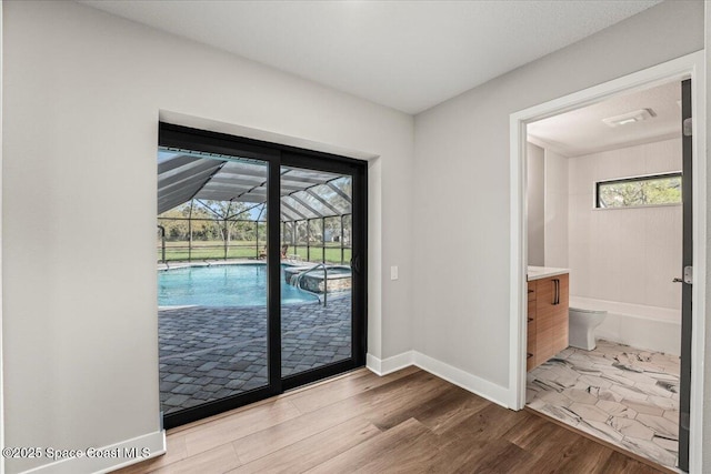 doorway featuring a sunroom, baseboards, and wood finished floors