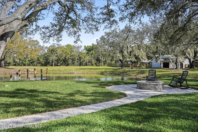 view of home's community with a water view, a fire pit, and a lawn