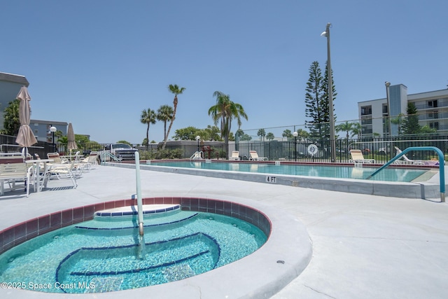 community pool with fence, a hot tub, and a patio