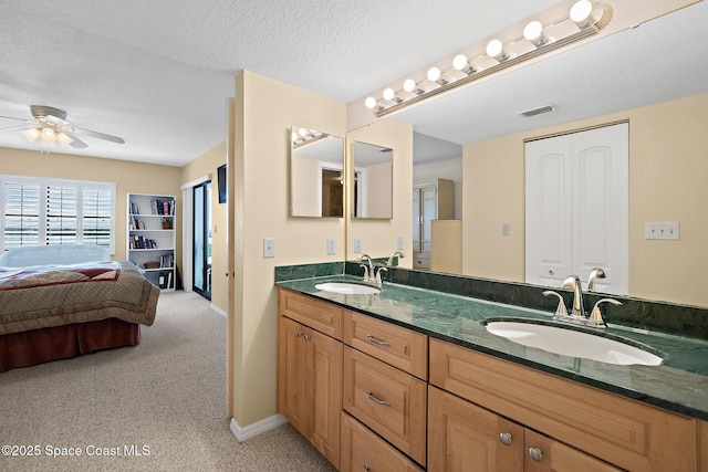 ensuite bathroom featuring a textured ceiling, double vanity, a sink, and visible vents