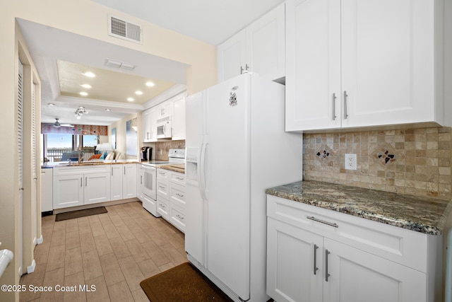 kitchen with a tray ceiling, visible vents, backsplash, white cabinetry, and white appliances