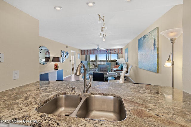 kitchen featuring stone countertops, a ceiling fan, open floor plan, a sink, and track lighting