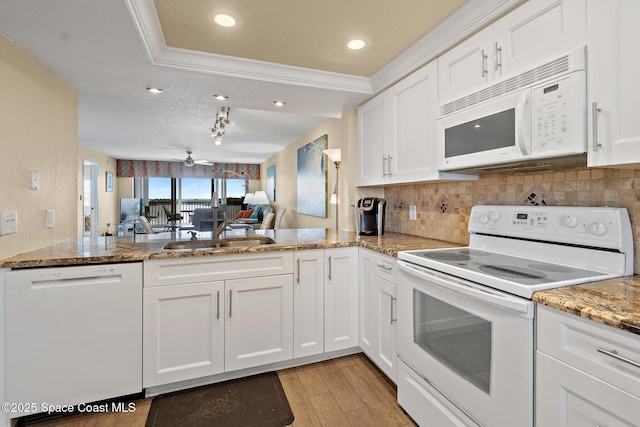 kitchen with a peninsula, white appliances, white cabinetry, and a sink