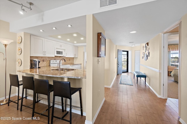 kitchen featuring decorative backsplash, white microwave, light wood-style flooring, light stone counters, and a sink