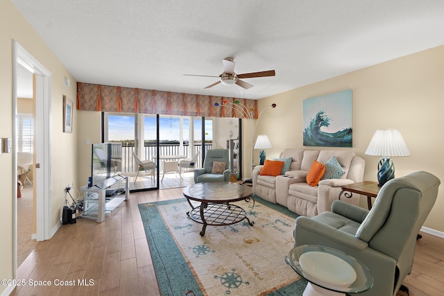 living room featuring a ceiling fan, a textured ceiling, baseboards, and wood finished floors