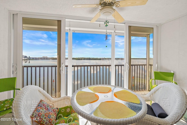 sunroom / solarium with a ceiling fan and a water view