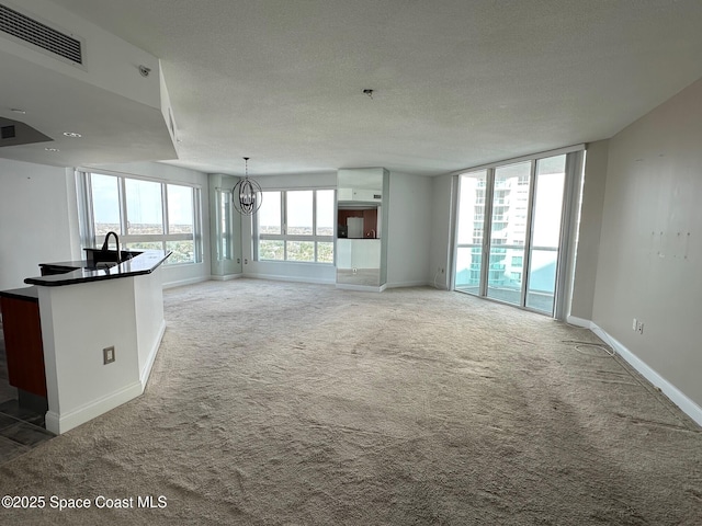 unfurnished living room with carpet, visible vents, a chandelier, and a textured ceiling