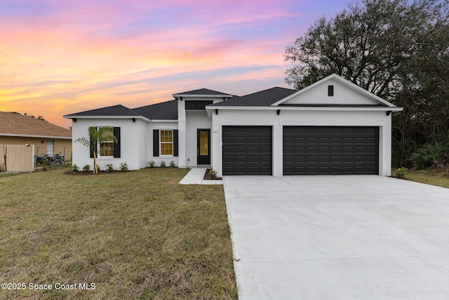 view of front of house featuring a garage, a lawn, concrete driveway, fence, and stucco siding