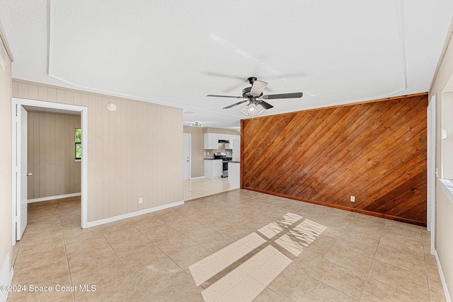 empty room featuring wooden walls, light tile patterned flooring, a ceiling fan, and baseboards