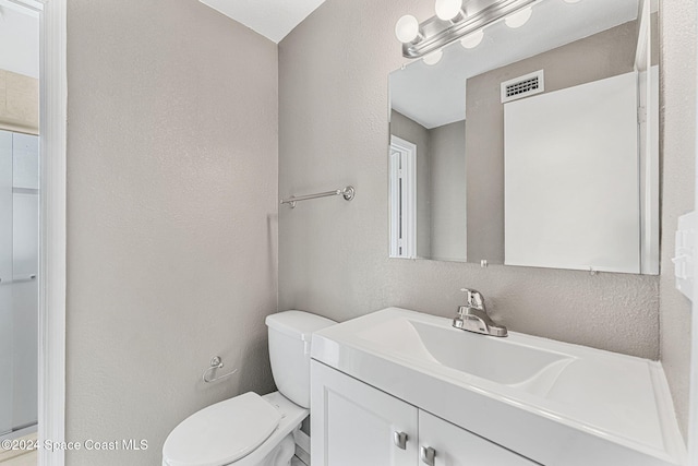 bathroom with visible vents, a textured wall, vanity, and toilet