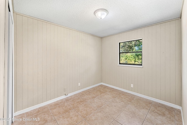 unfurnished room featuring a textured ceiling, light tile patterned floors, and baseboards