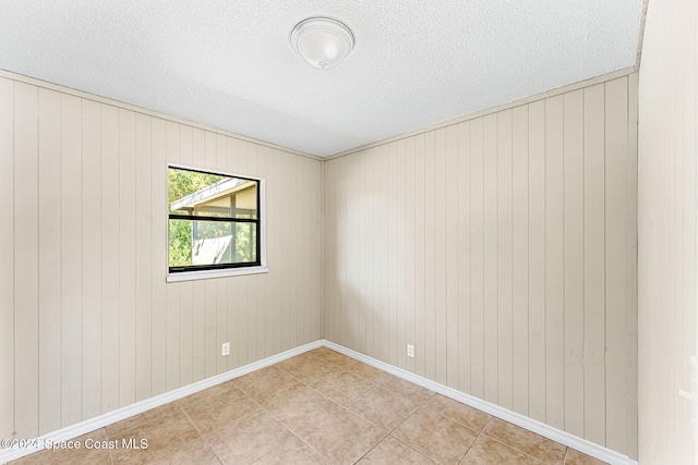 empty room featuring a textured ceiling, light tile patterned flooring, and baseboards