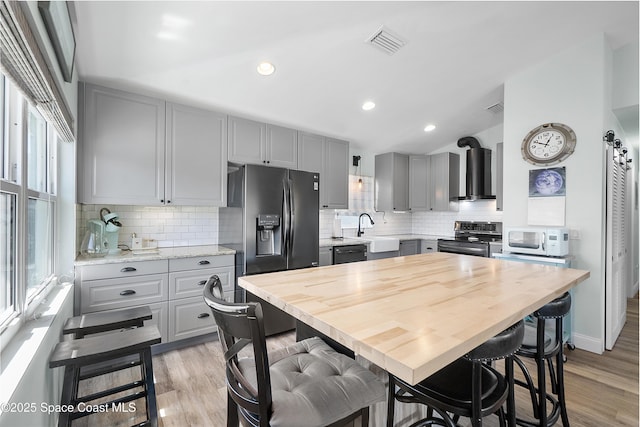 kitchen featuring gray cabinetry, a sink, wall chimney exhaust hood, black appliances, and light wood finished floors