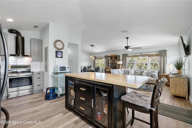 kitchen with white microwave, wood counters, electric stove, wall chimney range hood, and a kitchen bar